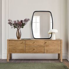 a wooden dresser with a mirror and flowers on it in front of a white wall