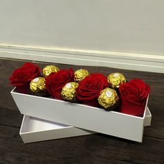 a white box filled with red roses and gold foil wrapped chocolates on top of a wooden floor