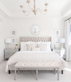 a large white bed sitting in a bedroom next to a chandelier and window