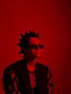 a man with spiked hair and sunglasses standing in front of a red background