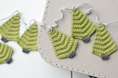 crocheted christmas tree ornaments are displayed on a white surface with stitched cord