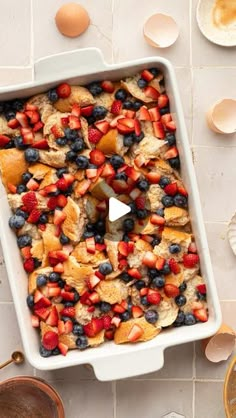 a casserole dish filled with fruit on top of a table next to eggs