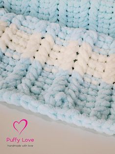 a blue and white crocheted blanket on top of a table next to a pink heart