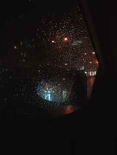 rain is pouring down on the windshield of a car at night with street lights in the background