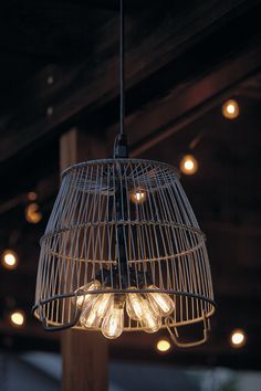 a bird cage hanging from the ceiling with light bulbs on it's sides and lights in the background