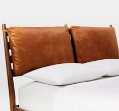 a bed with white sheets and brown leather headboard