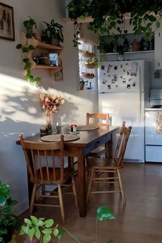 a kitchen with a table and chairs next to a refrigerator filled with potted plants