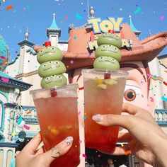 two people holding up glasses with drinks in front of a toy story land sign and confetti