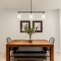 a dining room table with two chairs and a vase on the top, in front of three framed pictures