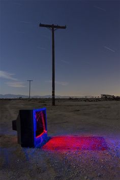 an old tv sitting in the middle of a dirt field next to a telephone pole