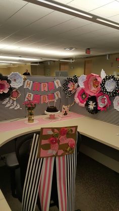 an office cubicle decorated with pink and black paper flowers, striped ribbon, and happy new year's decorations