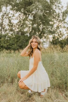 a woman in a white dress is sitting on the grass and smiling at the camera