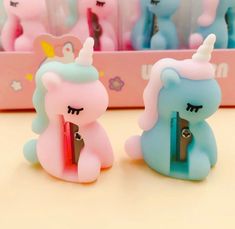 two little unicorn erasers sitting on top of a table next to a pink box