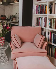 a pink chair and ottoman in front of bookshelves