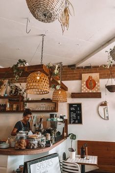 a person sitting at a counter in a restaurant with lots of plants hanging from the ceiling