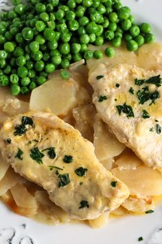 a white plate topped with meat and potatoes covered in sauce next to pea green peas