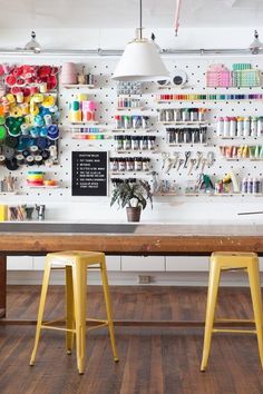 a table with two stools in front of it and a shelf full of craft supplies on the wall