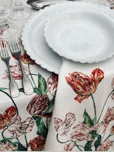 the table is set with white plates and silverware on it, along with floral - print napkins