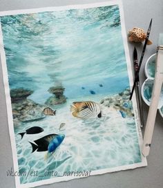 an underwater scene with watercolors and paintbrushes on the table next to it