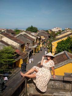 a woman sitting on top of a wooden fence next to buildings and trees in the background