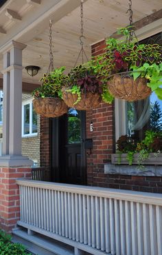 three hanging baskets filled with plants on the front porch