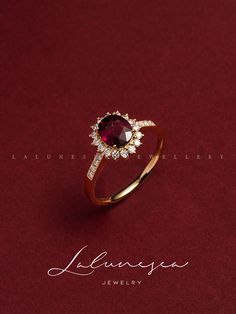 an engagement ring with a red stone surrounded by white diamonds on a red velvet background