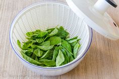 fresh basil leaves in a white strainer on a wooden counter top with a blender nearby