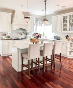 a kitchen filled with lots of white furniture and decor on top of a hard wood floor