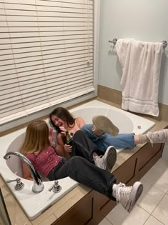 two women sitting in a bathtub with their feet up on the edge of the tub