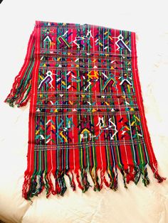 a red blanket with multicolored designs on it sitting on a white bed sheet