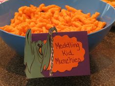 a blue bowl filled with cheetos next to a sign that says meddling kid munchies