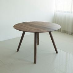 a round wooden table sitting on top of a white tile floor next to a window