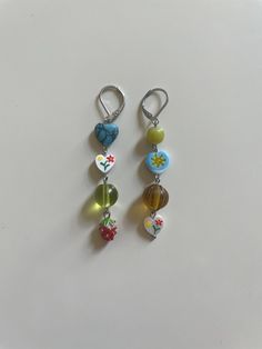 two pairs of earrings with flowers and hearts hanging from hooks on a white table top