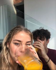 a man and woman drinking orange juice from a glass in front of their faces,