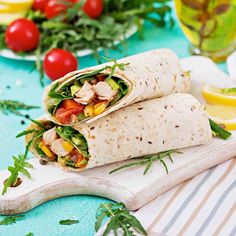 two wraps filled with chicken and vegetables on a cutting board next to lemon wedges