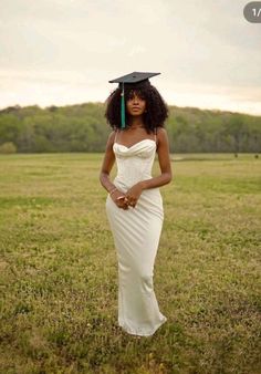 a woman in a white dress and black graduation hat standing in a field with her hands on her hips