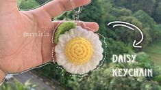 a hand holding a crocheted flower keychain in front of some trees