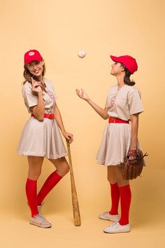 two young women dressed in baseball uniforms, one holding a bat and the other throwing a ball