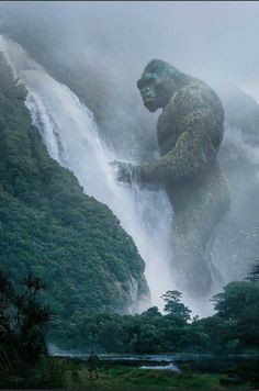 a giant gorilla standing in front of a waterfall with mist coming off the mountain side