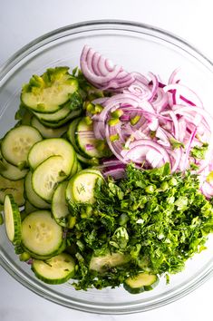 a glass bowl filled with sliced cucumbers, onions and green leafy vegetables