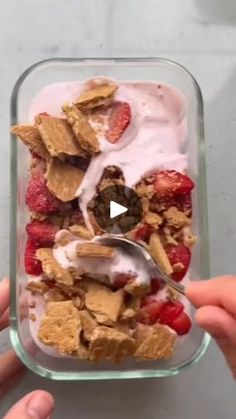 someone is holding a spoon over a bowl of granola and strawberries with yogurt