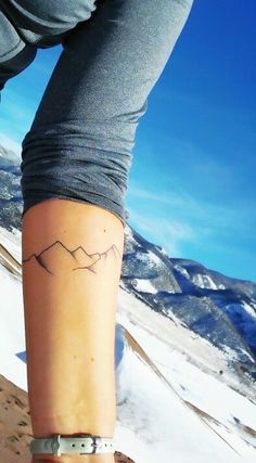 a person with a tattoo on their leg standing in the middle of a snow covered mountain