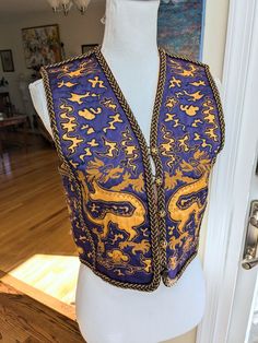 Late 1960s Saint Laurent Rive Gauche Purple and Gold Dragon Vest. This vest is decorated with gold dragons and clouds that are cut out of the purple background. The trim is braided brown cord and wrapped gold metal and is applied to all of the seams as well as center front. The front closes with five buttons that have gold filagree covers. One of the filagree button covers is missing, but otherwise the vest is in excellent condition. Size 34 Bust: 34" Waist: 33" Shoulders: 14" Length: 17.5" Arlington Va, Gold Dragon, Late 1960s, Button Covers, Rive Gauche, Purple Background, Vest Outfits, Purple Backgrounds, Womens Vest