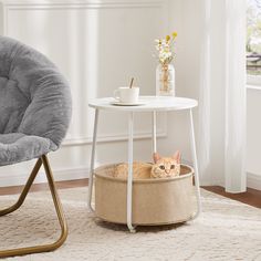 an orange cat sitting in a basket under a table next to a chair and coffee cup