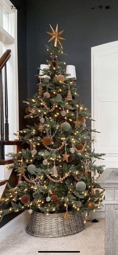 a christmas tree with lights and ornaments in a basket on the floor next to stairs