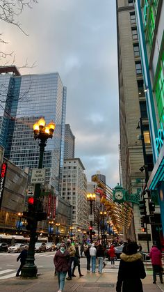 people are walking on the sidewalk in front of tall buildings and street lights at dusk