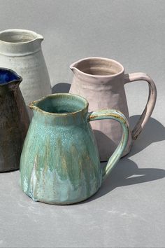 three ceramic pitchers sitting next to each other on a gray surface with one pitcher in the middle