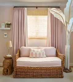 a living room with pink curtains and a wicker couch in front of a window