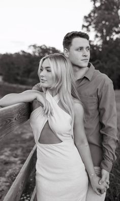 a man and woman standing next to each other on a wooden bridge in black and white