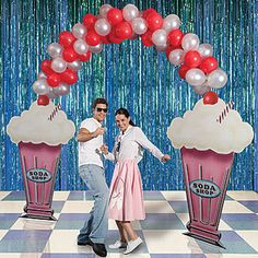 a man and woman posing in front of a photo booth with balloons on the wall